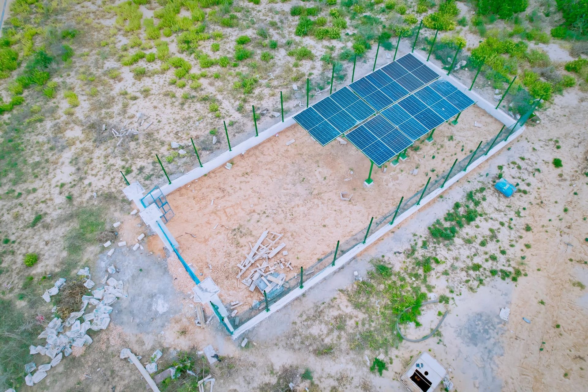 Aerial view of a fenced area in a desert landscape with solar panels installed on metal structures.